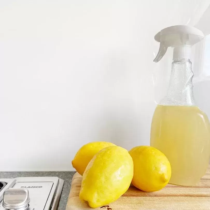 Cleaning solution next to lemons on a wooden cutting board.